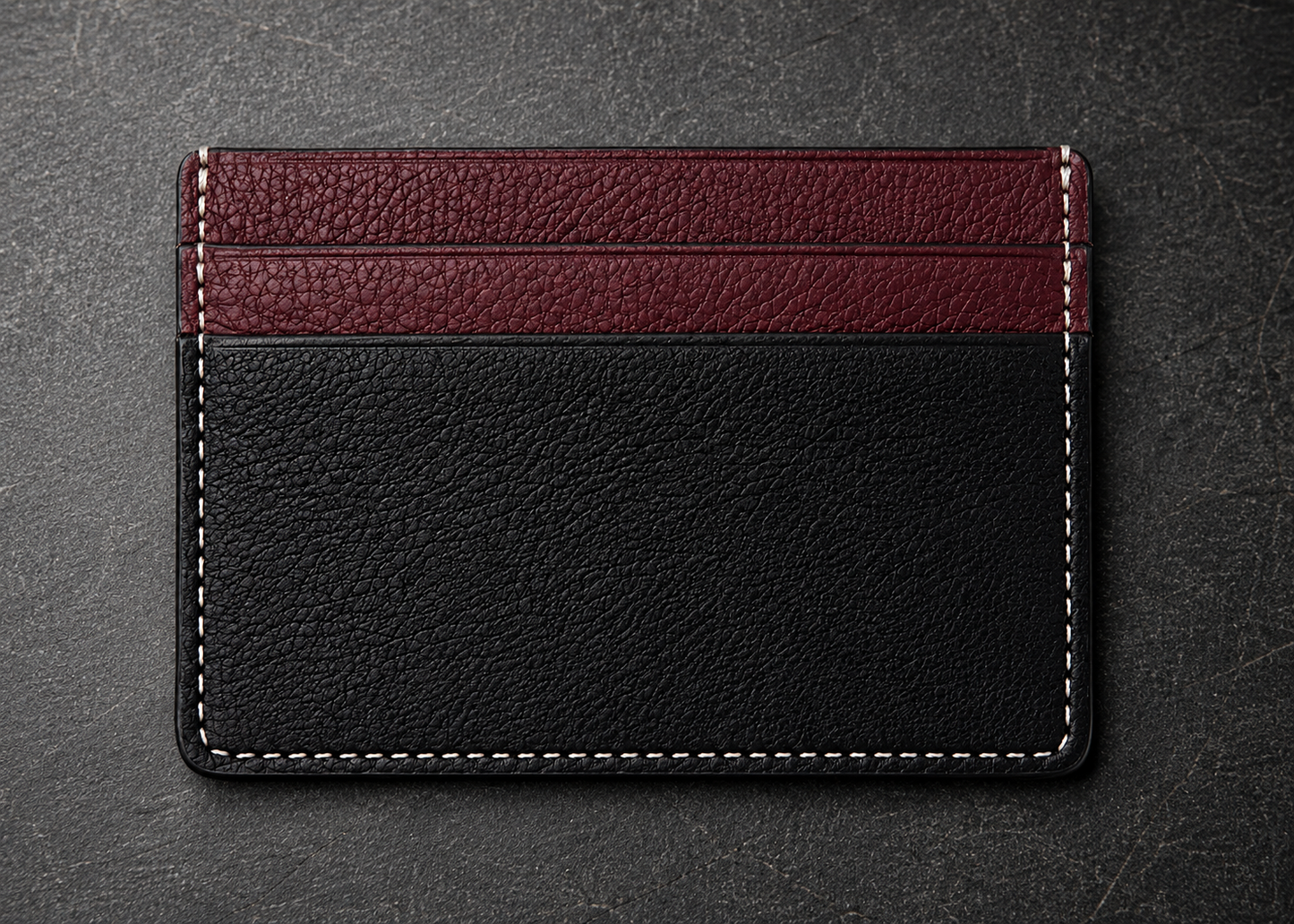 Two-tone leather cardholder with black and burgundy sections on a dark textured background
