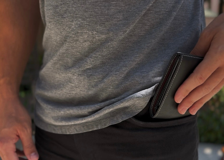 Person wearing a gray sleeveless shirt and black pants, holding a black wallet.